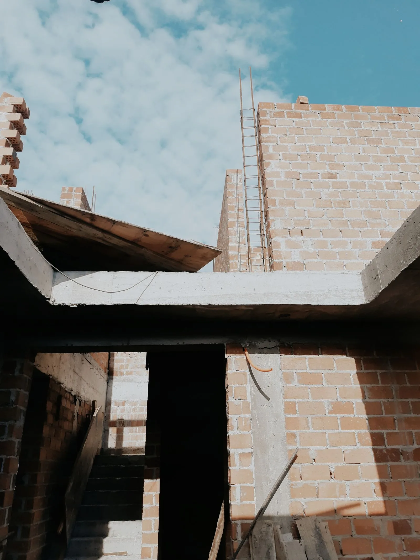 Casă în construcție din cărămidă, cu grindă de beton turnată, stâlpi cu armătură și cofraje de lemn.