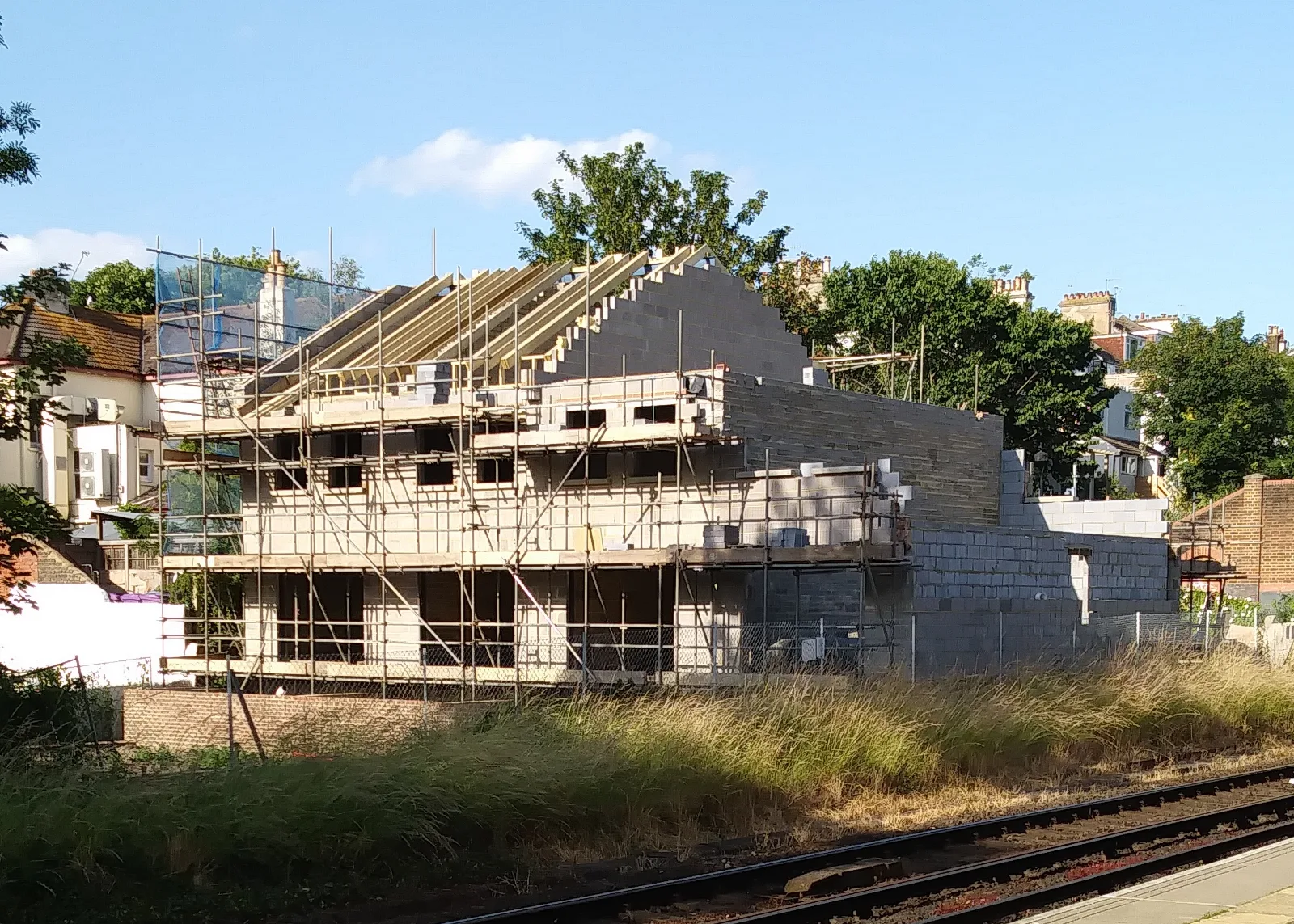 Casă cu pereți din blocuri de beton în construcție, cu schelă și căpriori de lemn pentru acoperiș.