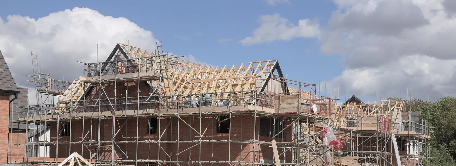 Case din cărămidă în construcție, cu schelă și ferme de lemn montate pe pereți pentru acoperiș.