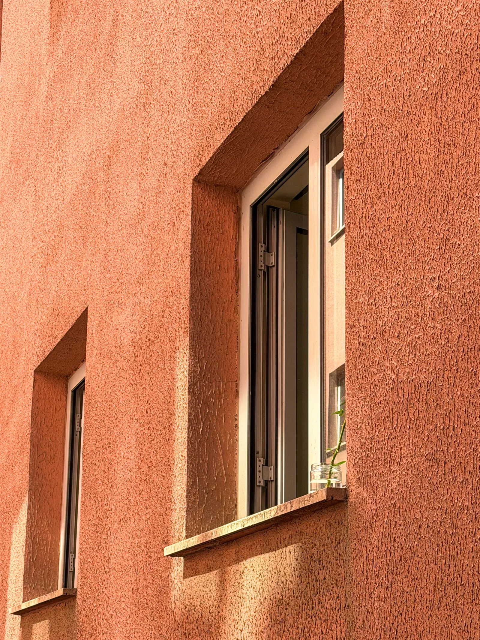 Fațadă cu tencuială decorativă texturată în ton teracotă, în jurul unei ferestre.