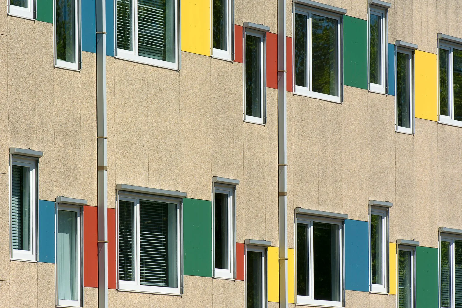 Fațadă cu tencuială texturată bej și panouri colorate lângă ferestre.