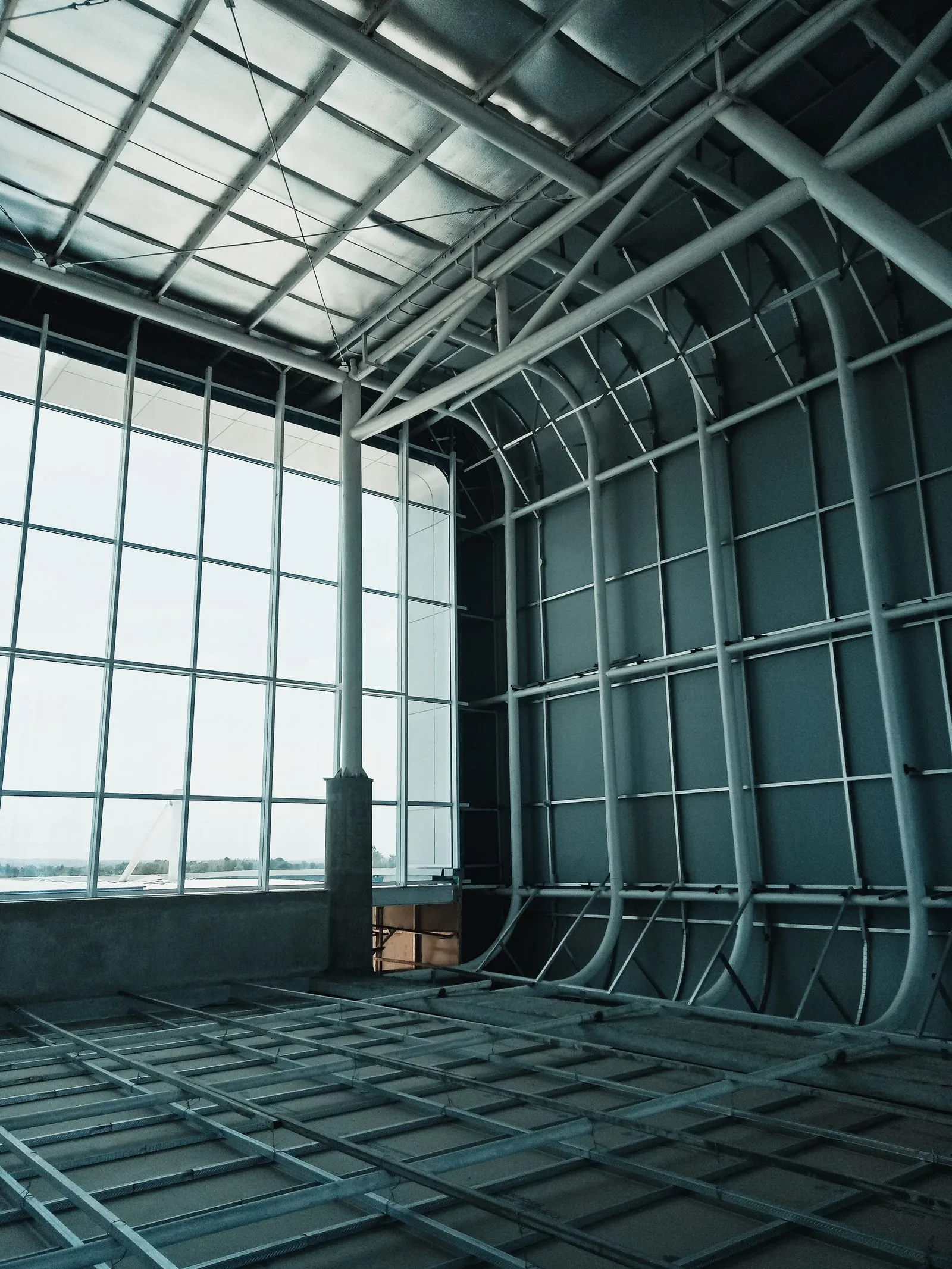 Structură metalică a unei hale în construcție, cu pane, rigle de perete și fațadă vitrată.