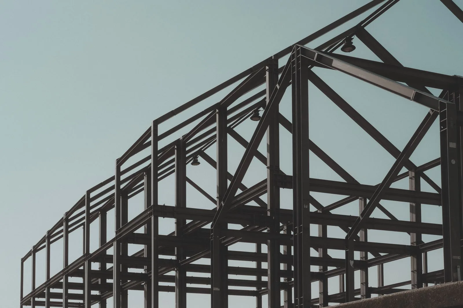 Structură metalică a unei hale industriale în construcție, cu stâlpi și grinzi de acoperiș pe cer senin.
