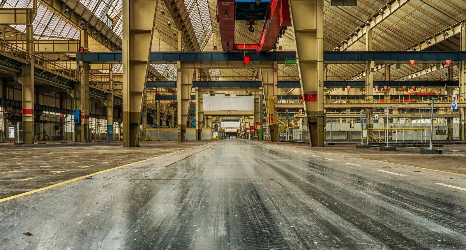 Interiorul gol al unei hale industriale pe structură metalică, cu stâlpi, grindă de pod rulant și luminatoare.
