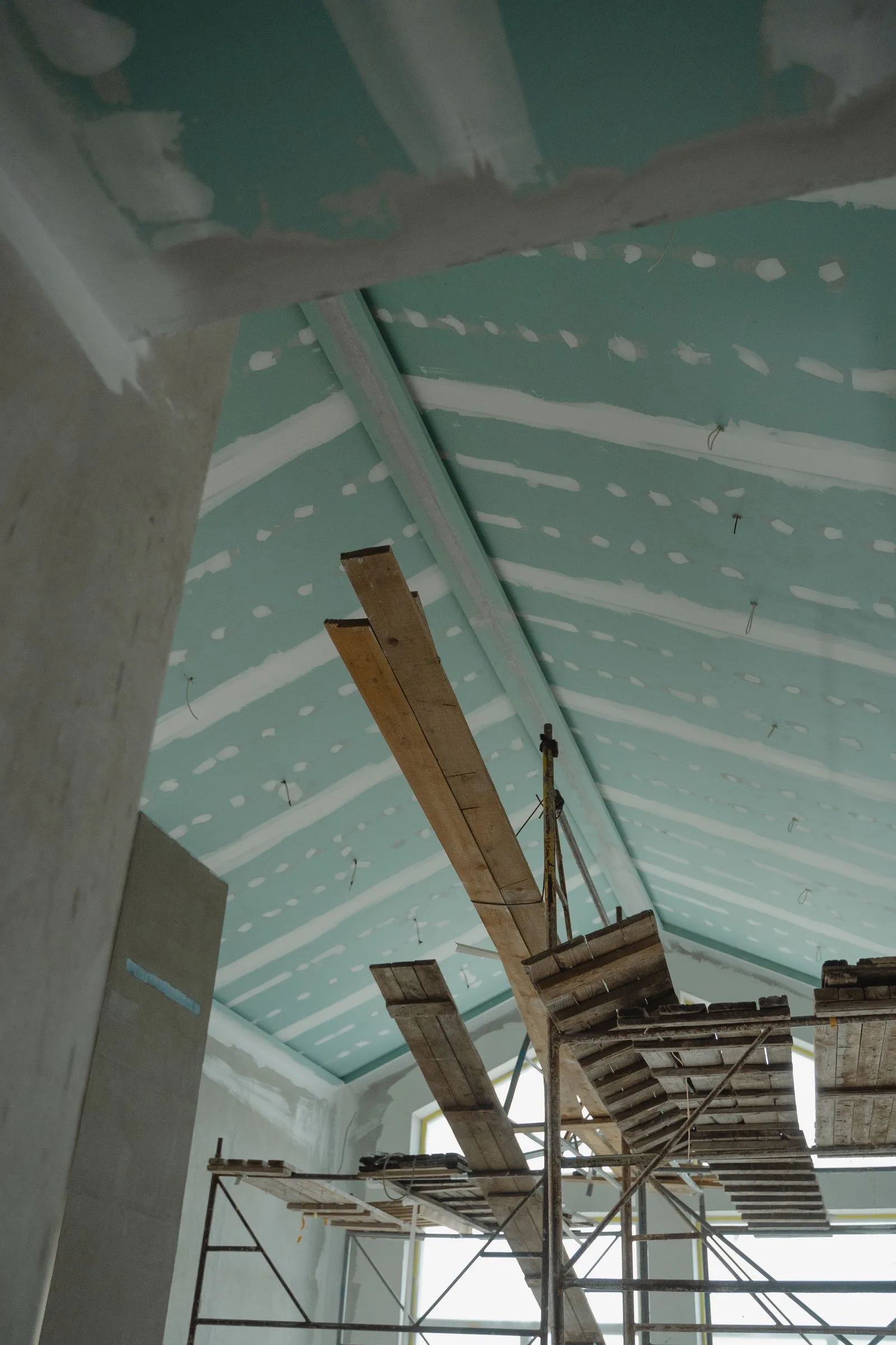 Tavan din gips-carton cu rosturi chituite, deasupra unei schele din lemn, într-o încăpere în renovare.