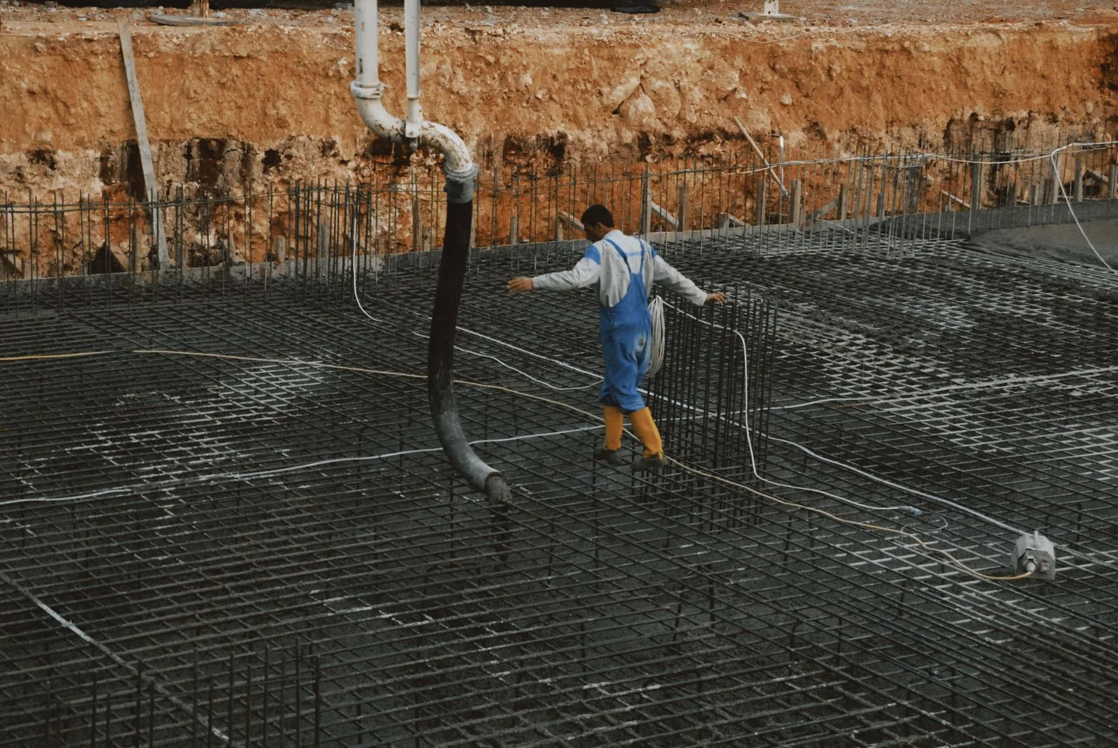 Muncitor dirijează furtunul pompei de beton peste plasa de armătură a unei fundații.