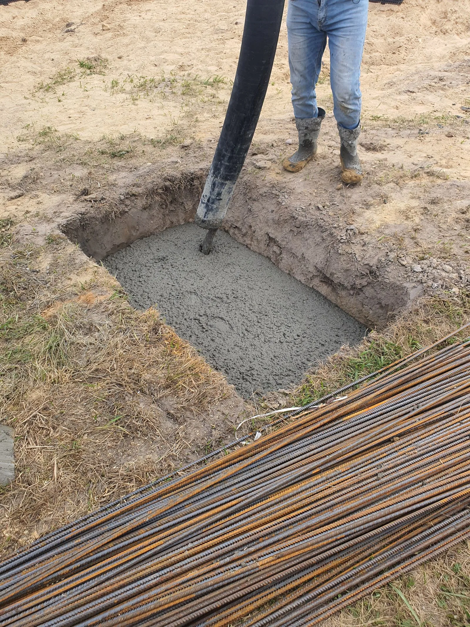 Beton turnat cu pompa într-o groapă de fundație, cu bare de armătură în prim-plan.