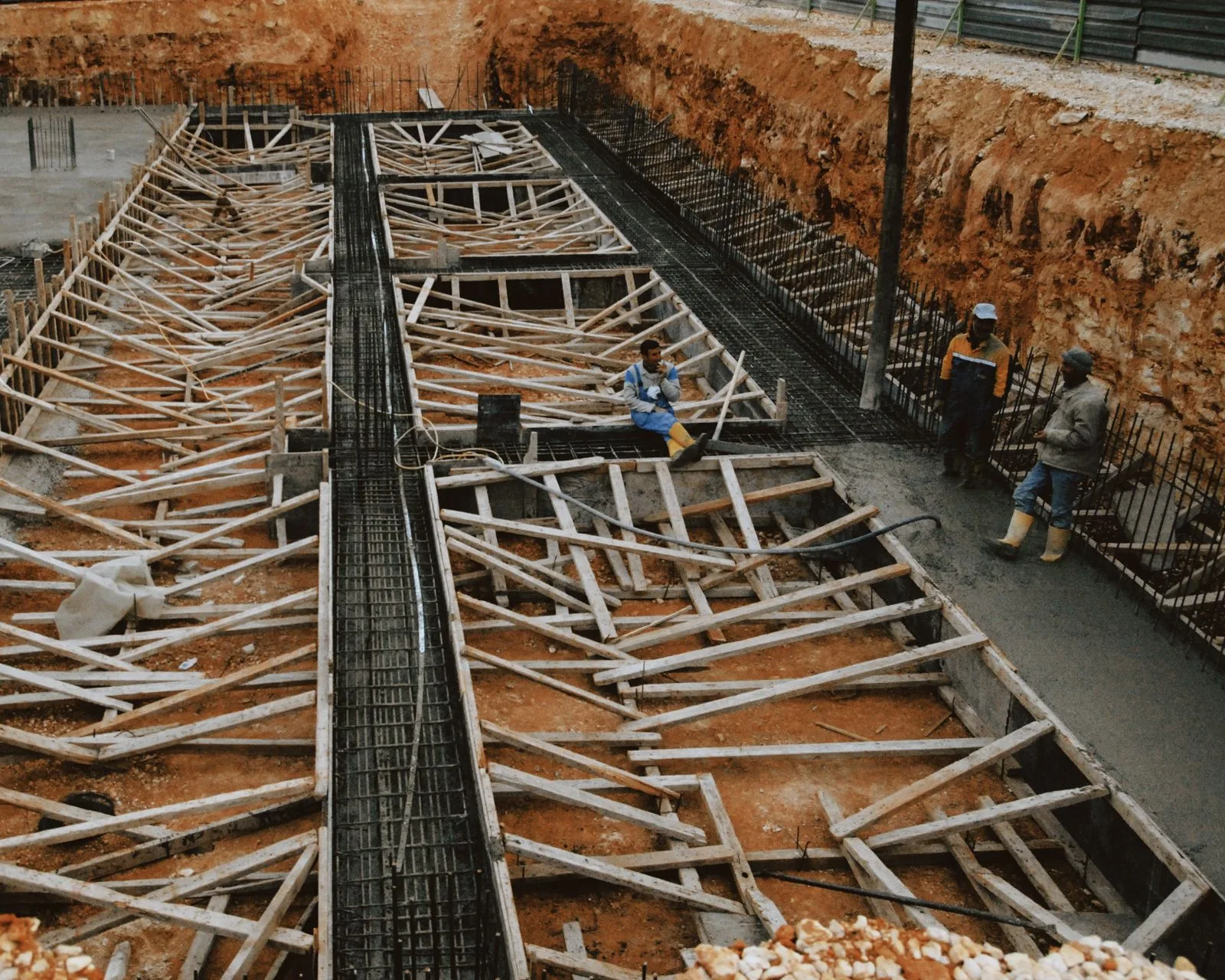 Cofraj din lemn și armătură pentru fundații continue într-o groapă excavată.